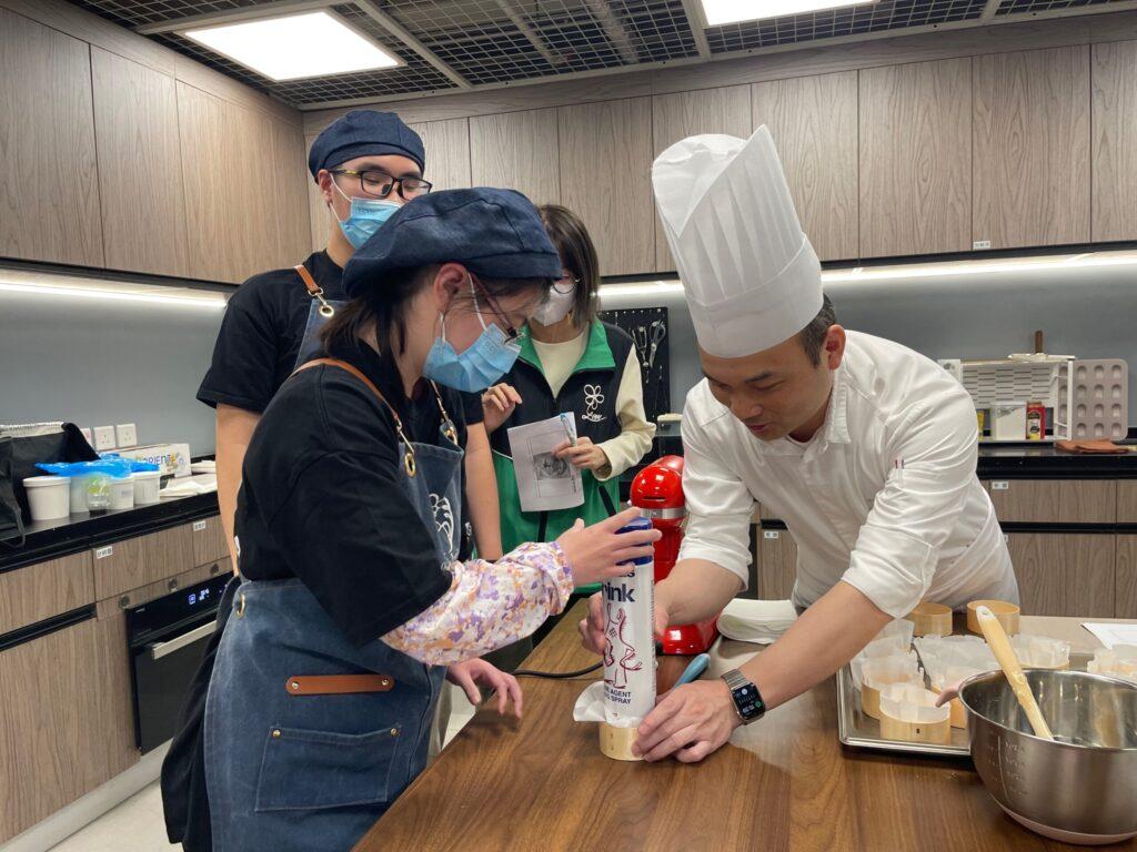 A young woman being taught by a chef in a kitchen