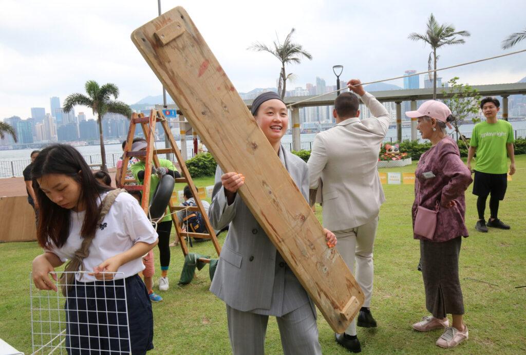 A woman holding a large piece of wood used in constructing a playground